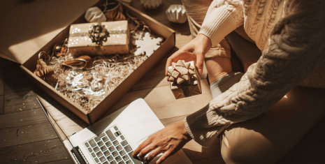 Woman seated on the floor with a gift box in hand and a laptop.