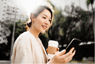 woman standing outside in a city holding a cup of coffee and looking at her mobile phone