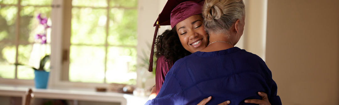 Girl in cap and gown hugging woman