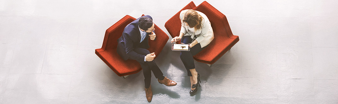 Man and women in conversation as they sit in red chairs.