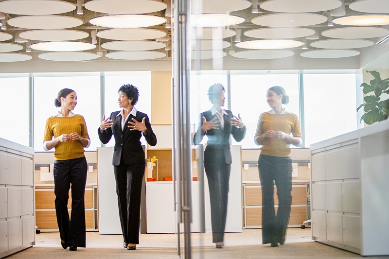 glass partition showing reflection of women in business attire walking in hallway