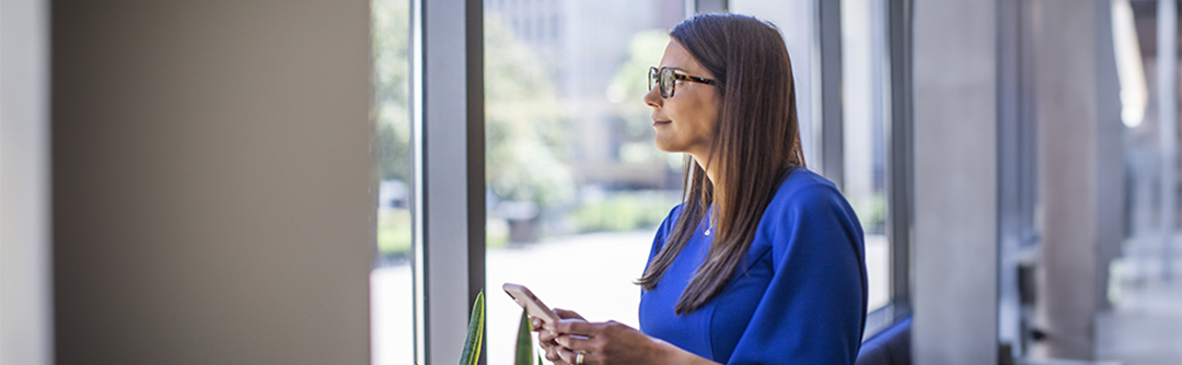 Woman holding cellphone in hands looking out a window