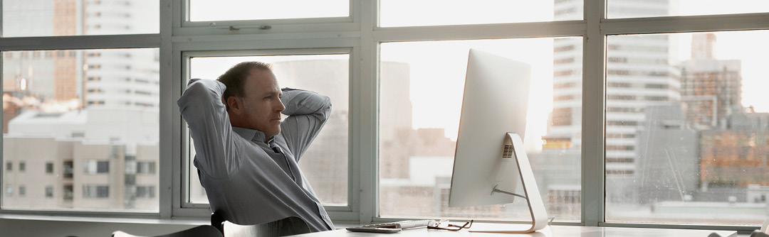 Man sitting in front of computer monitor with hands behind his head