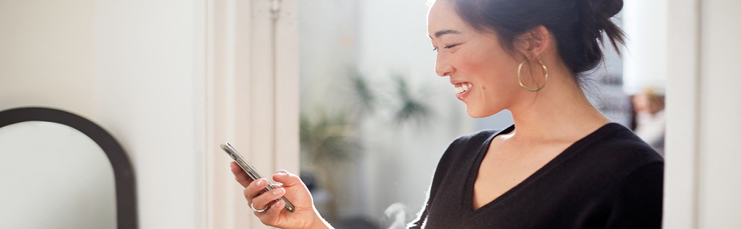 A young woman smiling and looking at her cell phone.