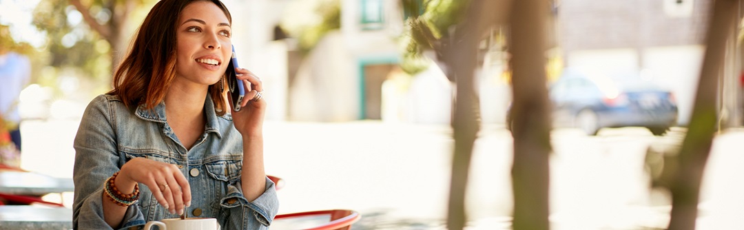 A young woman sits with her coffee and is talking on her cell phone.